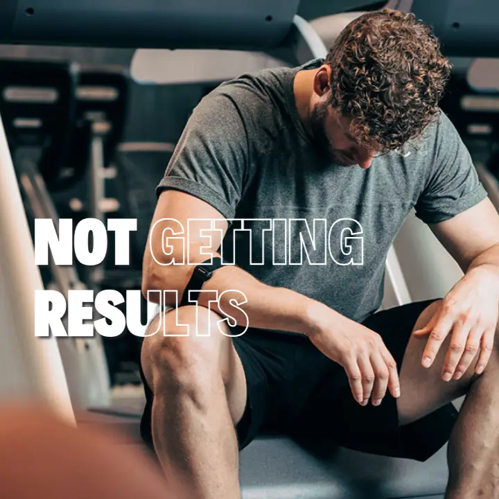 Frustrated man in gym attire looking at himself in the mirror, reflecting on lack of fitness progress.